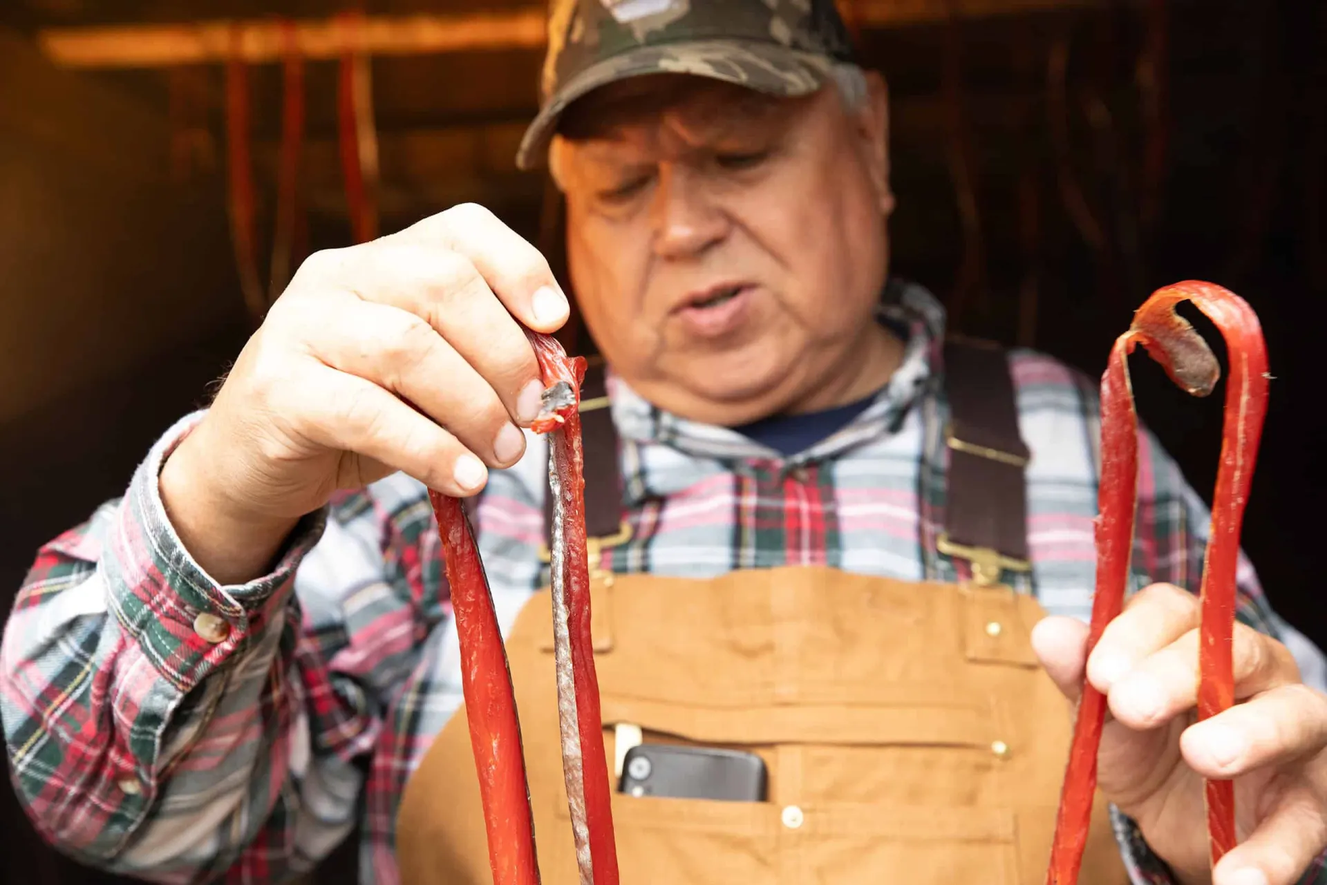 An elder in a camouflage cap holding strips of dried salmon